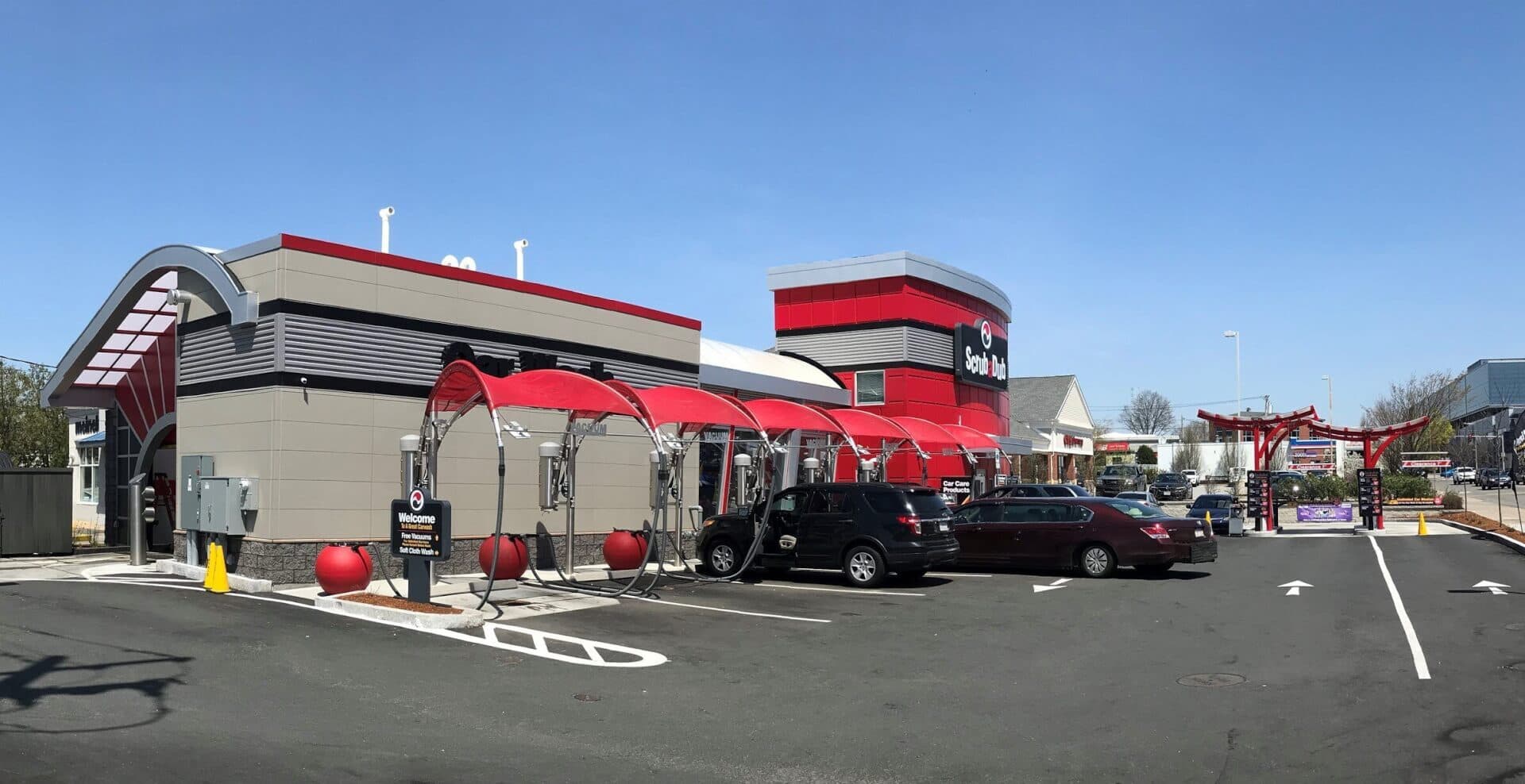ScrubaDub Brighton car wash with red vacuum canopies, red ball trash cans, and cars at the vacuum spots