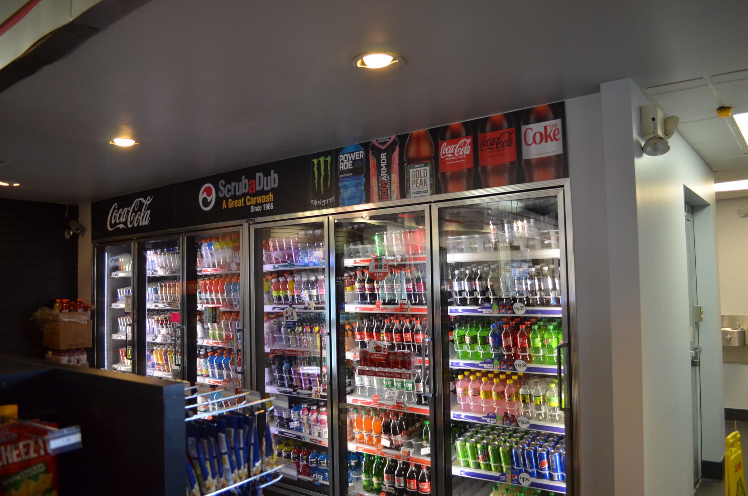 Wall of stocked drink coolers under a ScrubaDub A Great Carwash Since 1966 header