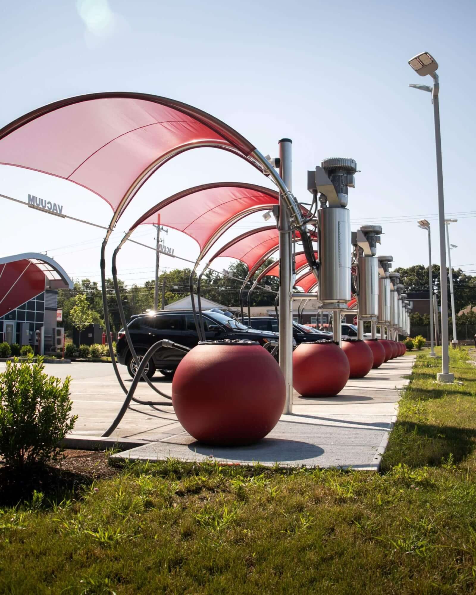 Row of red vacuum canopies with stainless vacuum units and red ball-shaped canisters at a ScrubaDub car wash