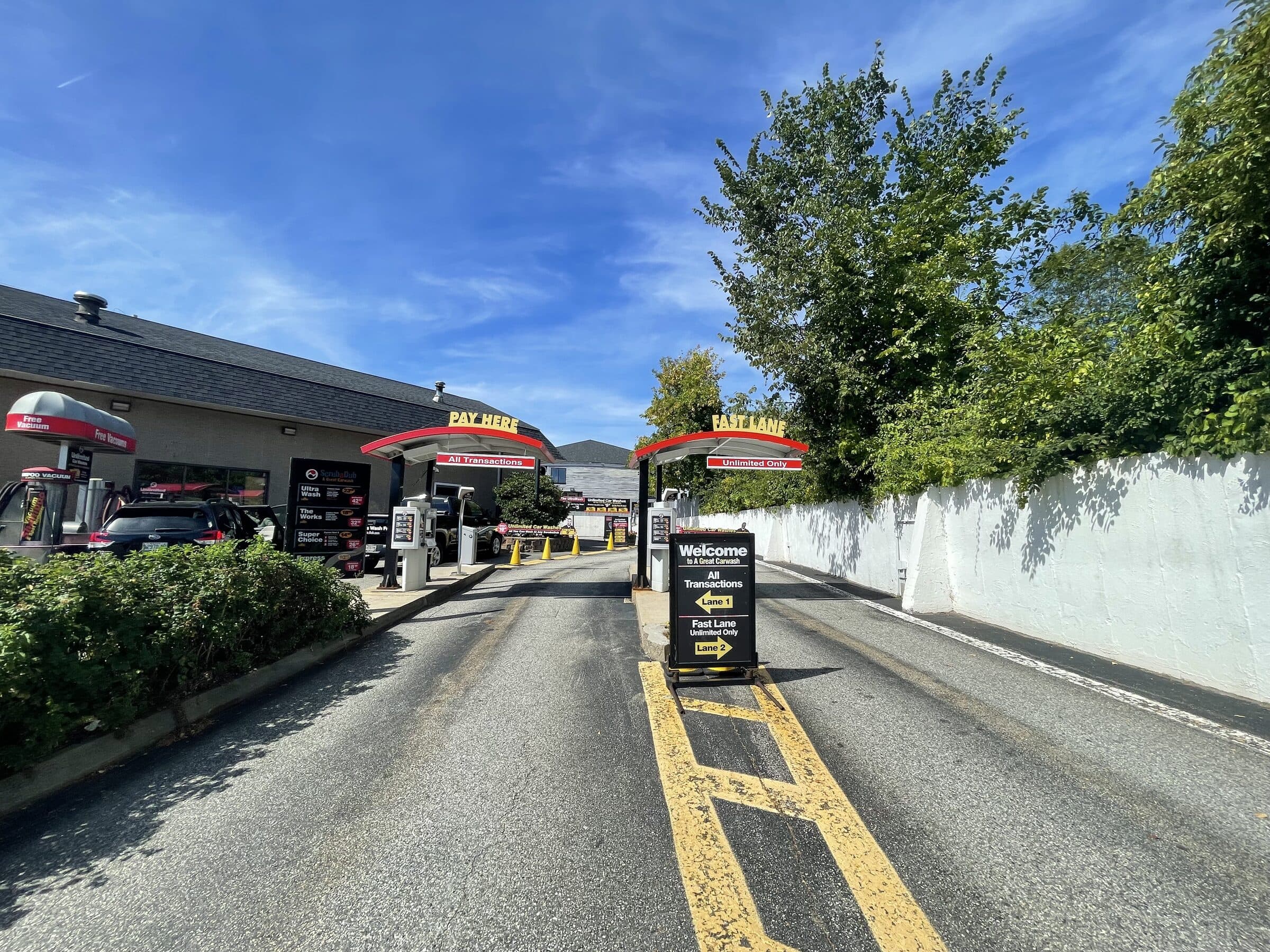 Two ScrubaDub entrance lanes under red canopies labeled "Pay Here" and "Fast Lane, Unlimited Only"