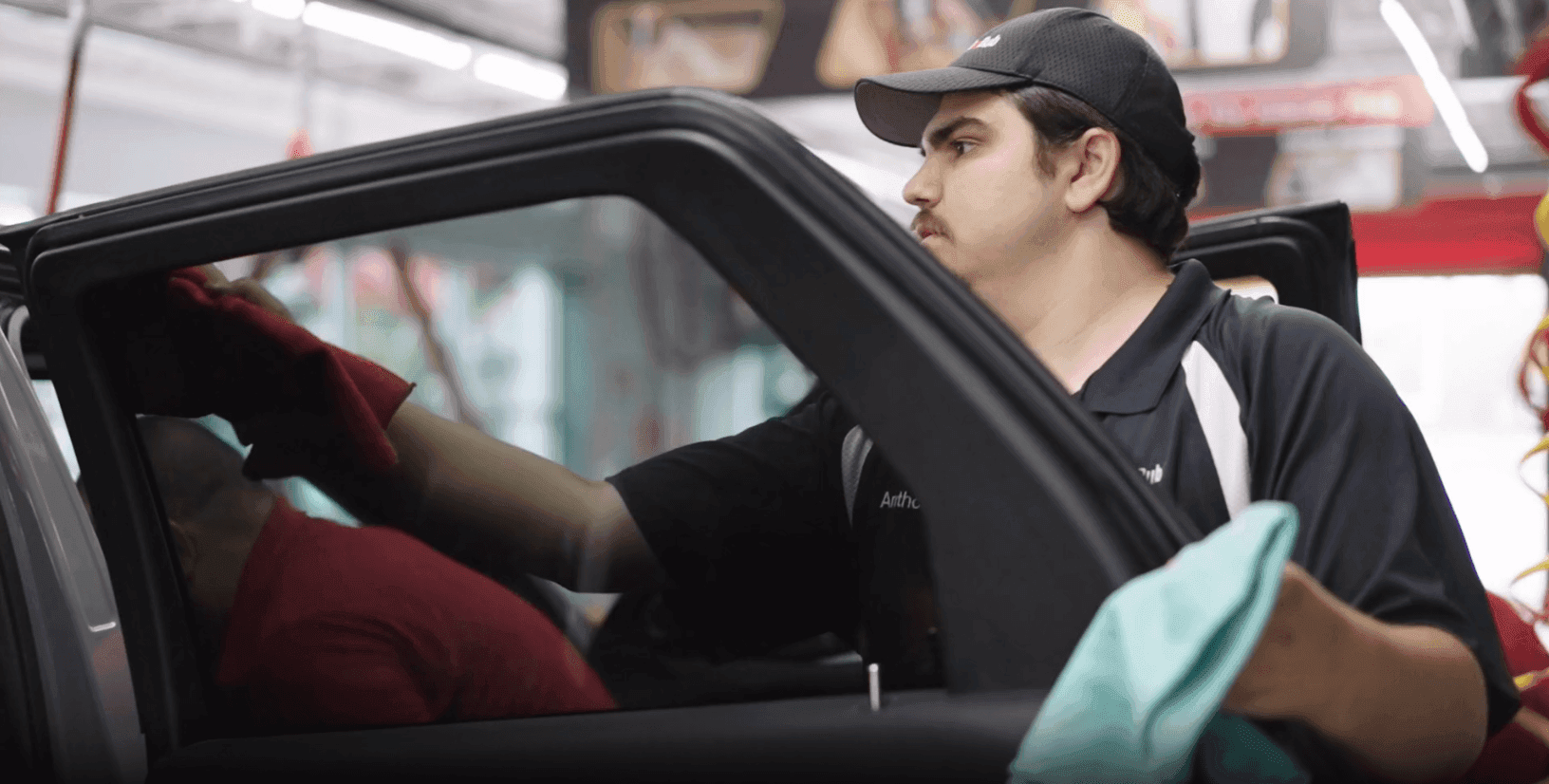 ScrubaDub attendant in a black cap wiping a car's door window with a towel