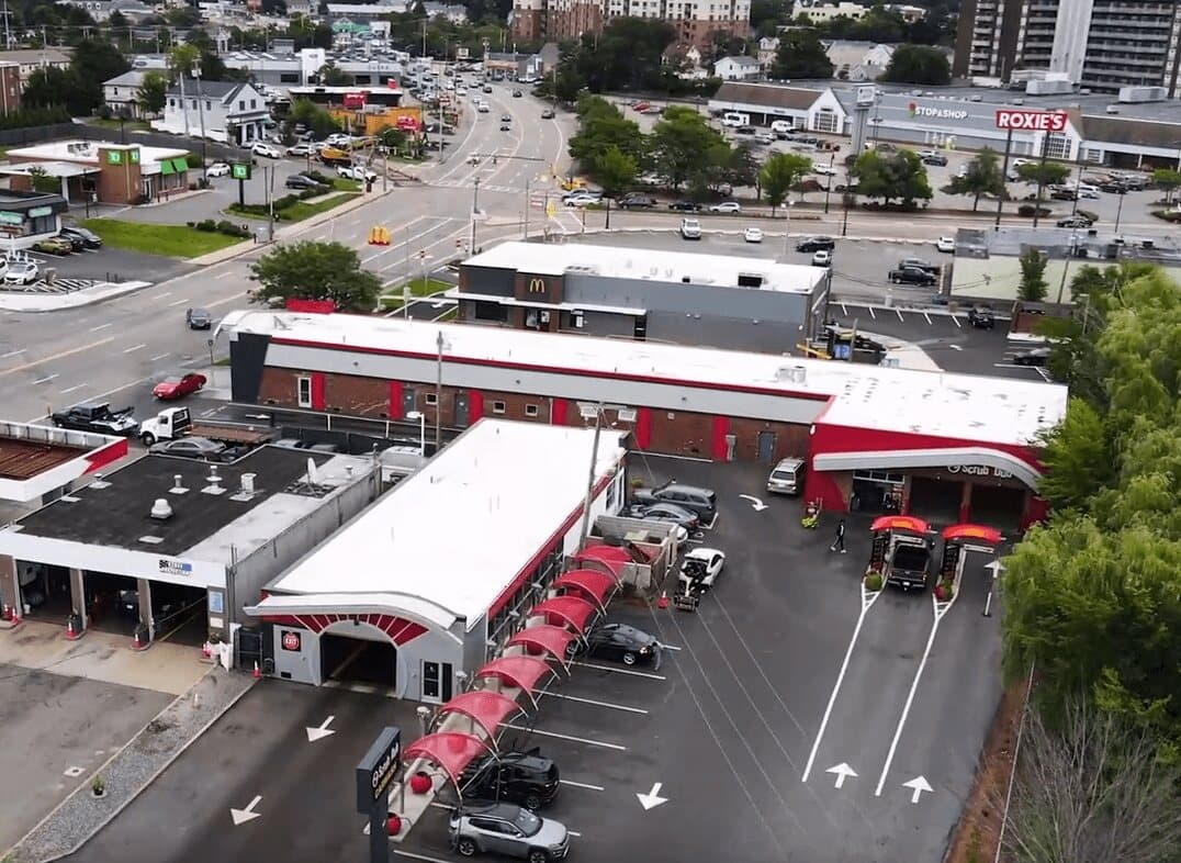 Aerial view of the ScrubaDub Quincy car wash with red vacuum canopies and pay lanes on a busy commercial street