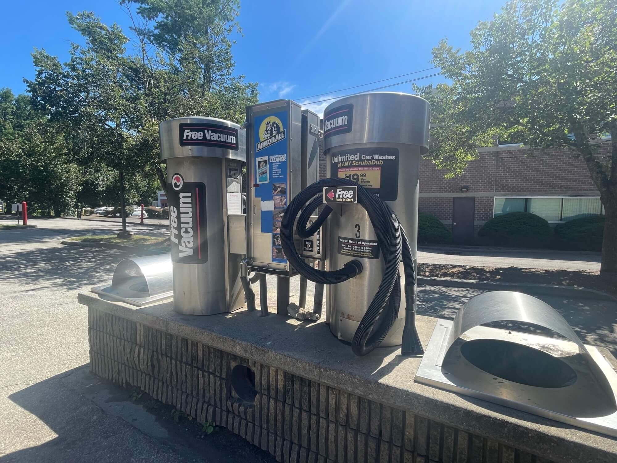 Stainless "Free Vacuum" stations with a coiled black hose and an Armor All vending machine