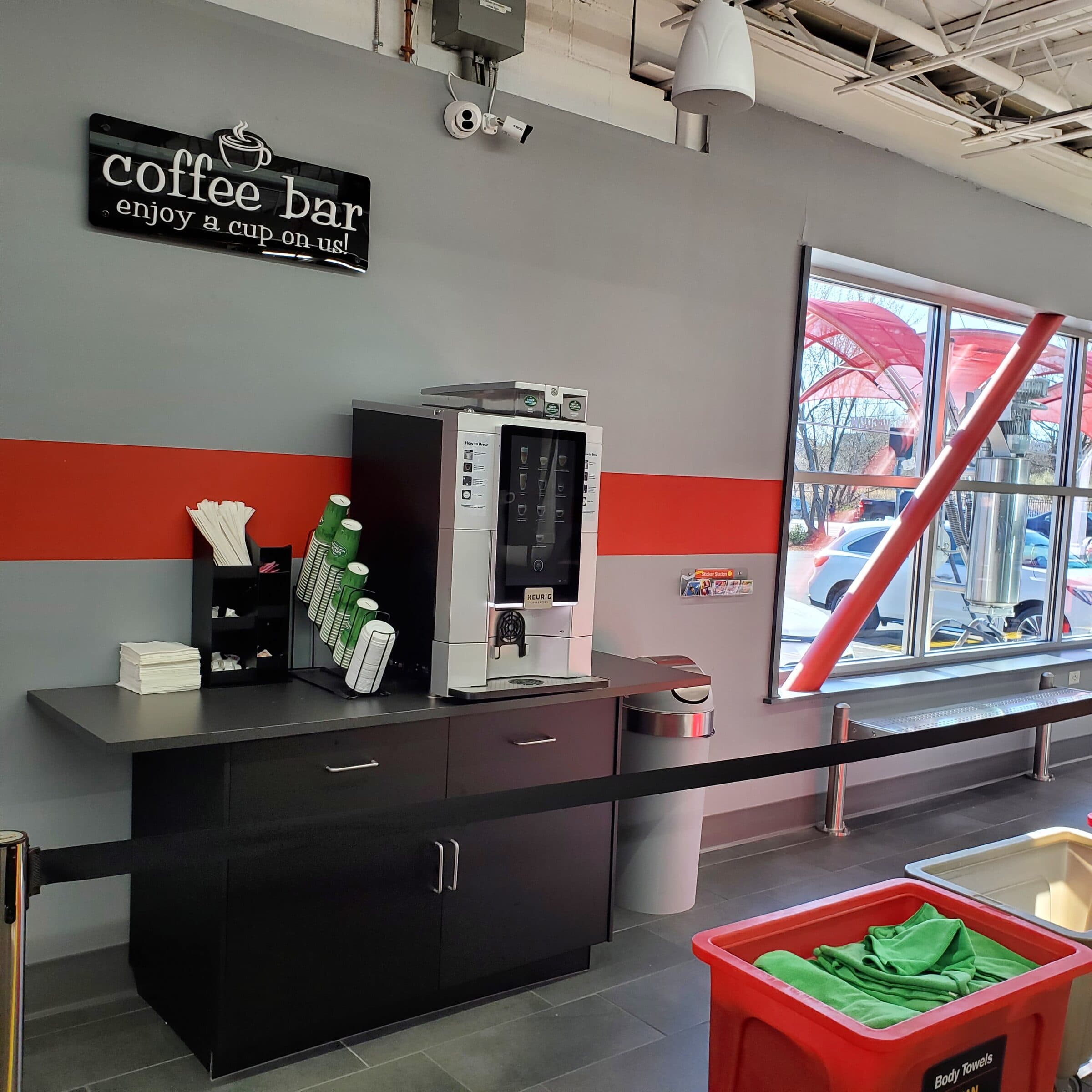 Free coffee bar with a Keurig machine under a sign reading "Coffee bar, enjoy a cup on us!"