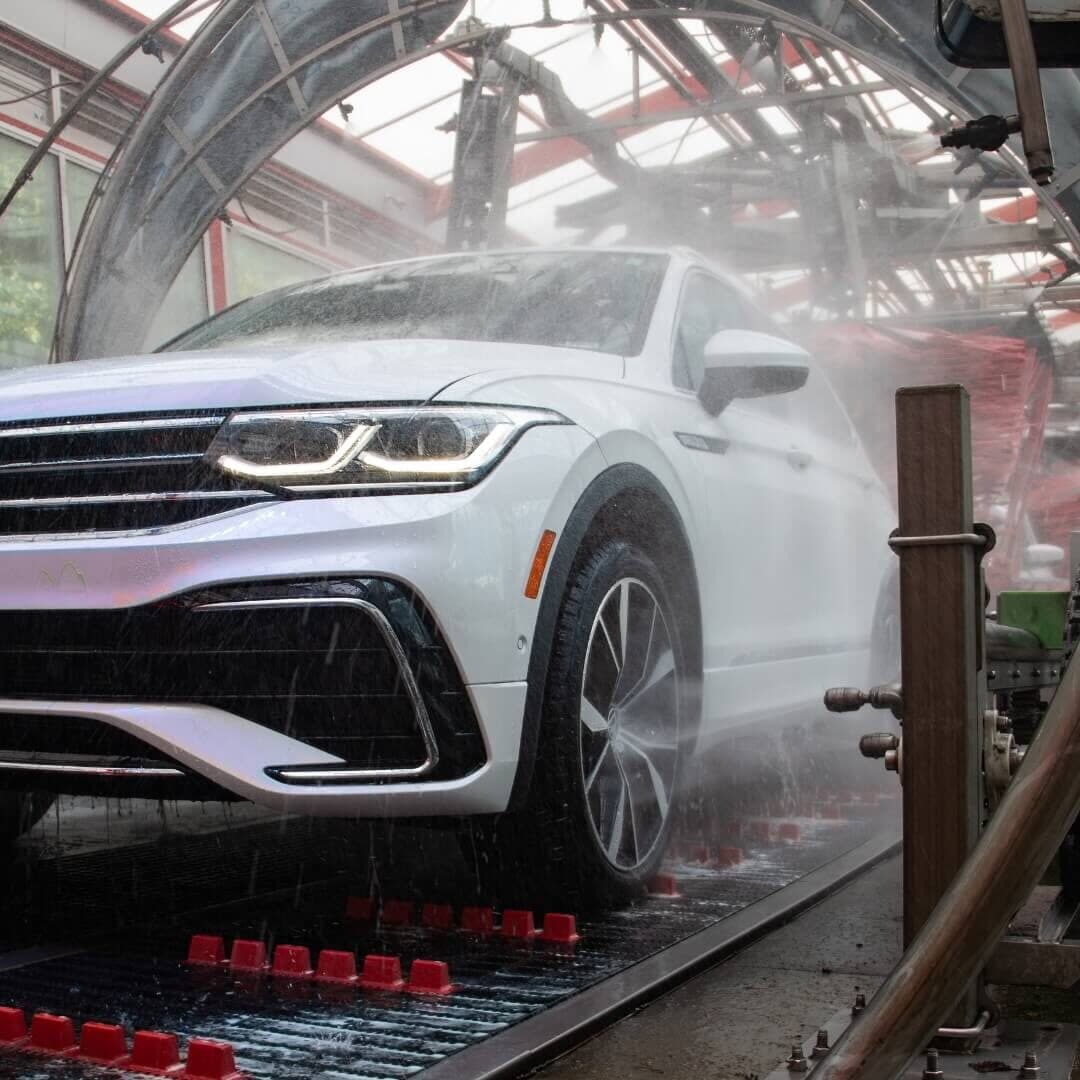 White SUV with headlights on moving through misty spray on a tunnel conveyor