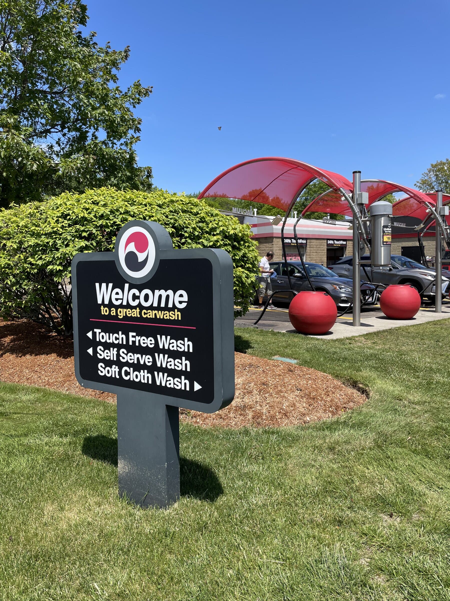 ScrubaDub welcome sign pointing to touch-free, self-serve and soft-cloth washes, with red vacuum canopies behind