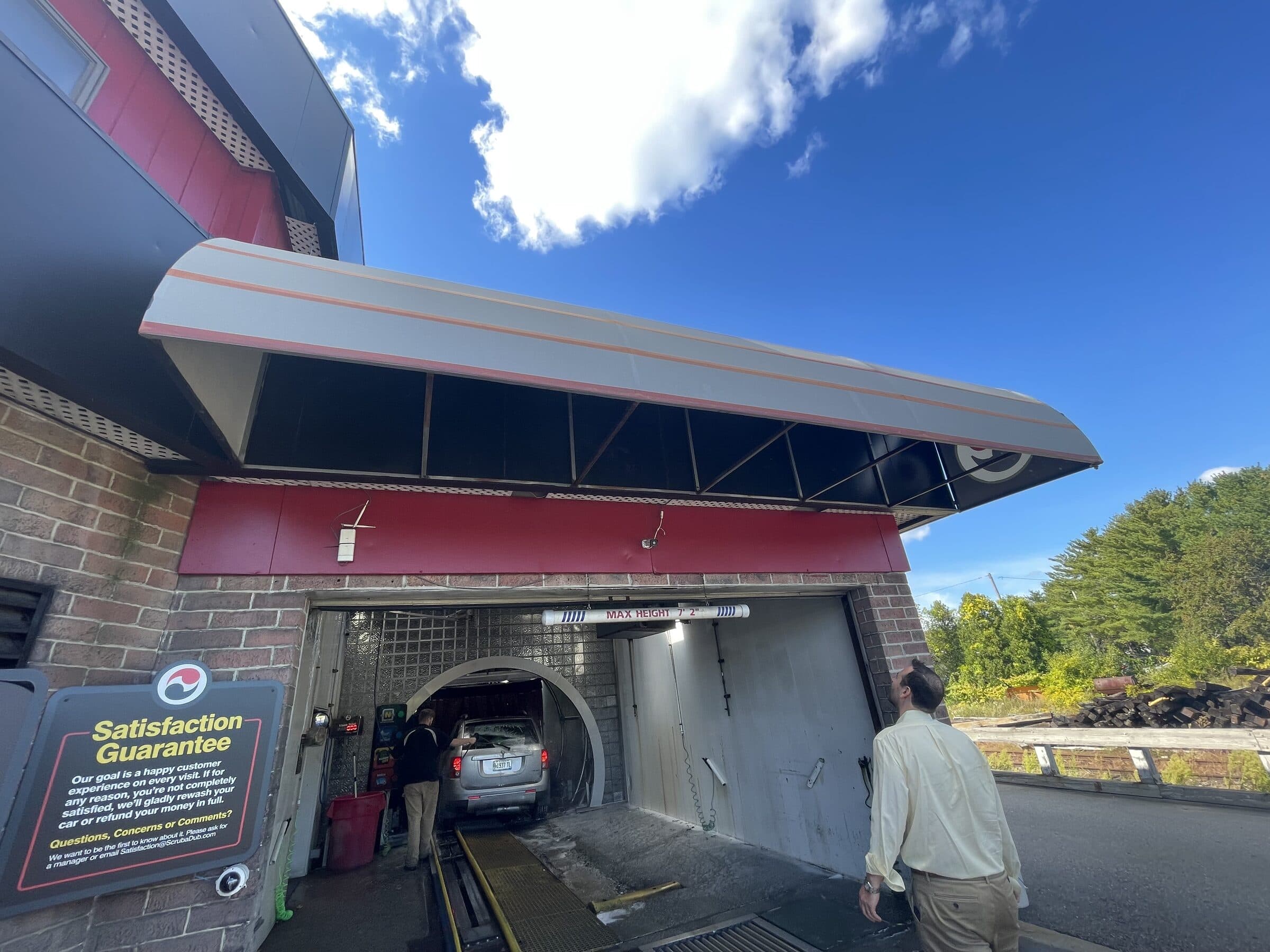 Attendant guiding an SUV into the ScrubaDub Portland tunnel entrance beside a Satisfaction Guarantee sign
