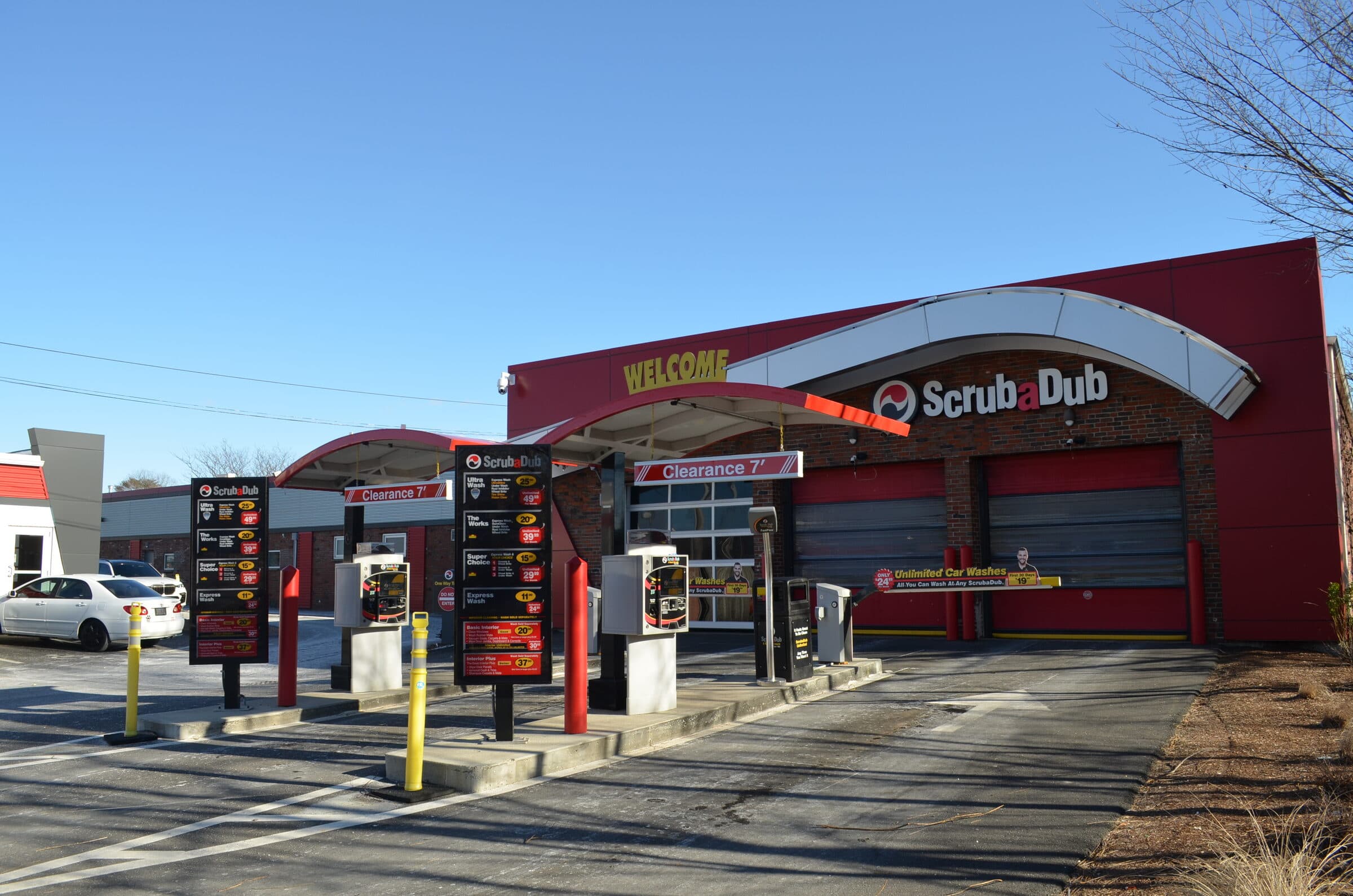 ScrubaDub pay lanes with wash menu boards, pay stations, and a red building with a "Welcome" sign